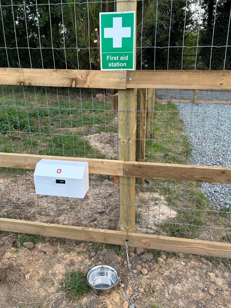 A first aid station sign and locked first aid box on the fence, with a water bowl below